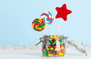 Various sweets assortment. Candy, bonbon, lollipop in glass can over blue background. With copy space